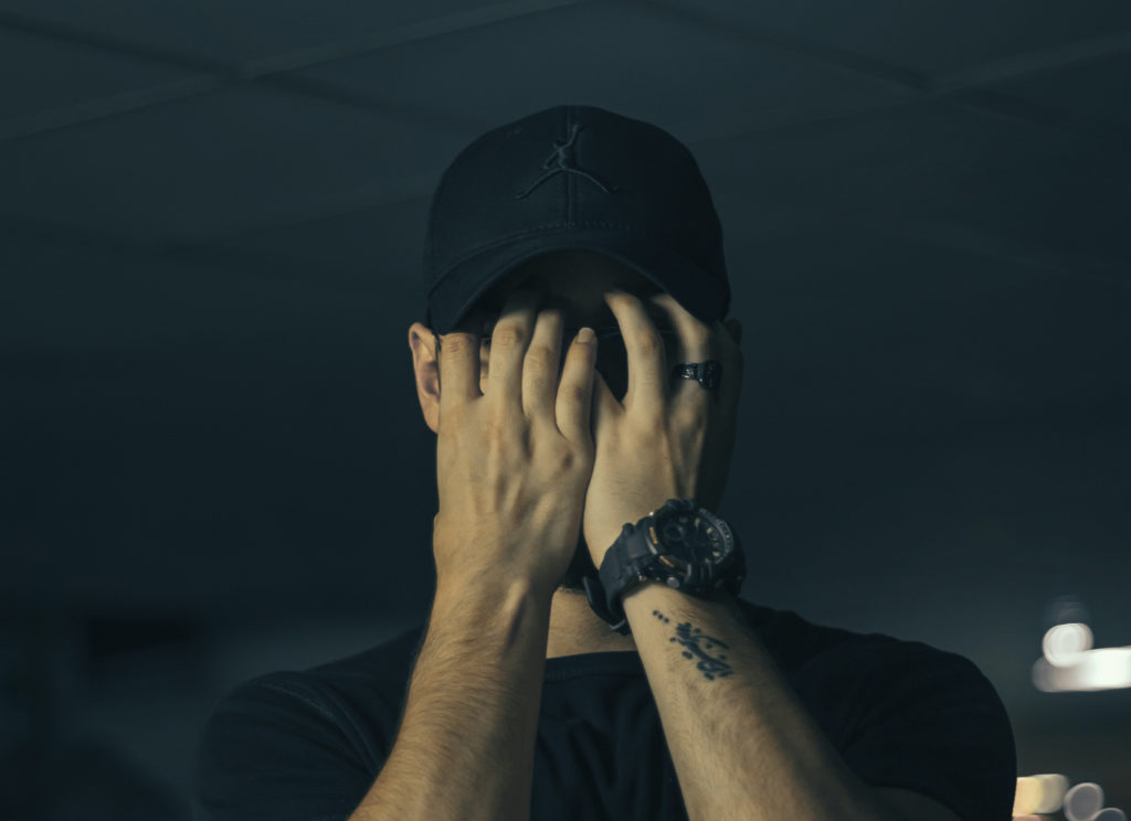 a man in a black hat holding his eyes in front of his face